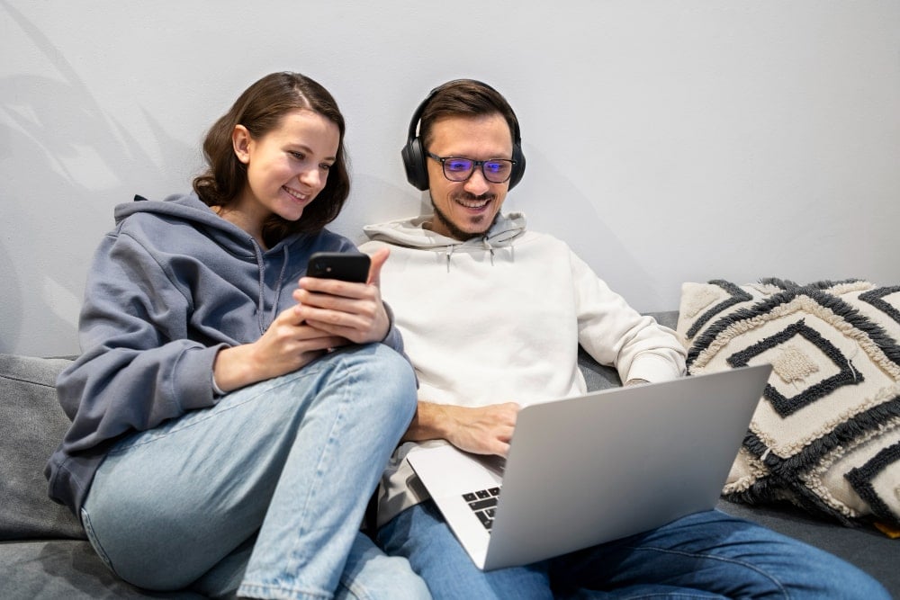 blij koppel op de bank met mobiele telefoon en laptop